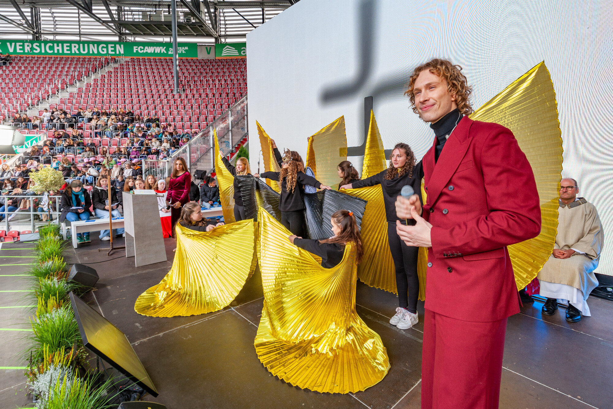 Musical-Darsteller im roten Anzug blickt zur Flügelchoreo, WWK Arena Augsburg / Schulwerk