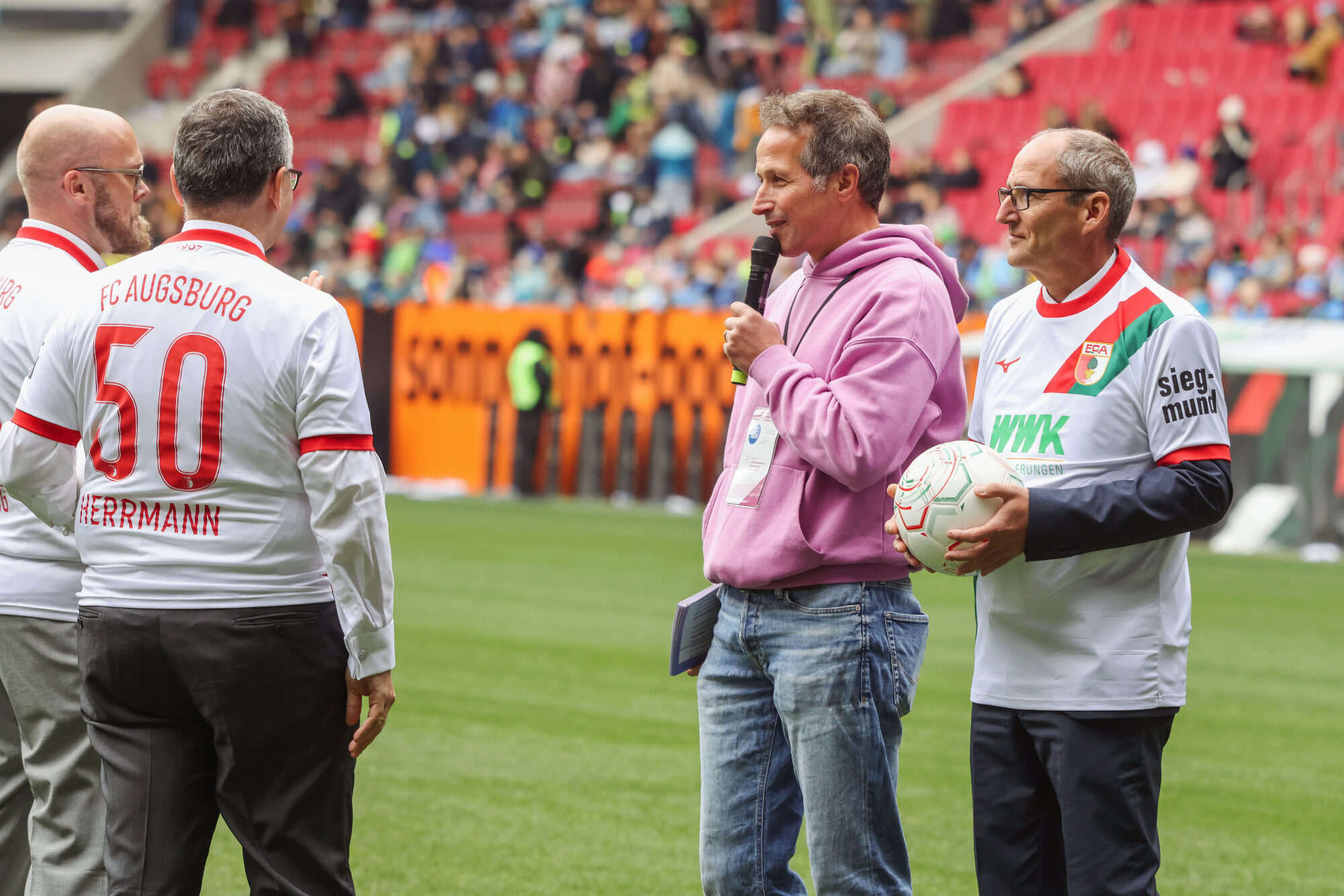 Willi Weitzel interviewt den Bischof mit Ball auf dem Rasen, WWK Arena Augsburg / Schulwerk
